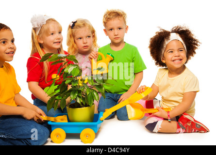 Group of kids playing on planting green spring tree sitting with watering can and cart to carry it Stock Photo