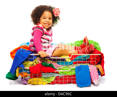 Cute little black girl sitting in the basket full of clothes with fuzzy hair and smile on her face, isolated on white Stock Photo