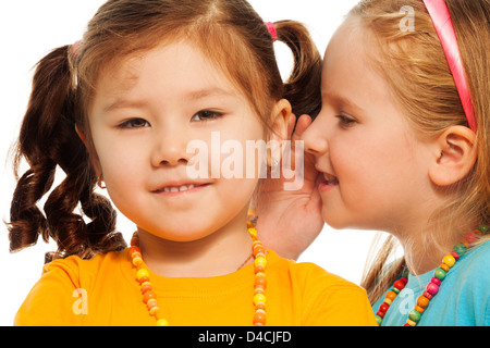 Closeup of two little 6-7 years old Asian and Caucasian girls gossip telling secrets mouse to ear, isolated on white Stock Photo