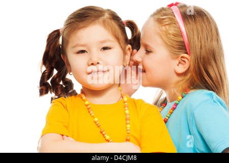 Close portrait of two little 6-7 years old Asian and Caucasian girls whisper telling secrets mouse to ear, isolated on white Stock Photo