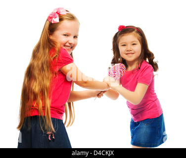 Two little six years old girls with long hair fighting over lollipop, Asian and Caucasian, isolated on white Stock Photo