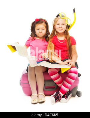 Two cute little exited girls sitting on suitcase with map preparing to travel wearing snorkel and mask, isolated on white Stock Photo