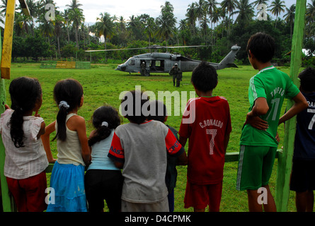 Local Children Watch a Member from Helicopter Sea Combat Squadron 23 “Wild Cards” Carry Float Coats for Passengers Stock Photo