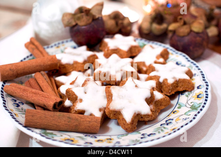 Star-shaped cinnamon biscuits and cinnamon sticks on a plate Stock Photo