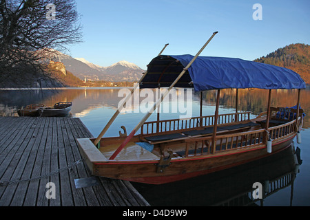 A Pletna a covered wooden rowing boat  with snow capped mountains on Lake Bled Slovenia Europe Stock Photo