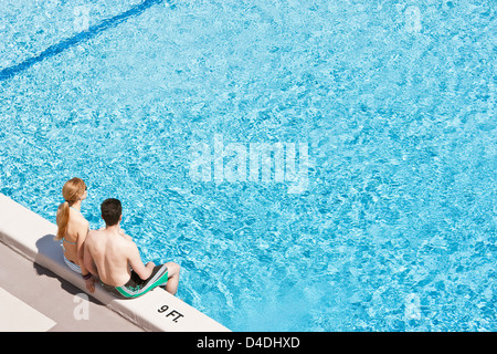 A young couple wearing bathing suits, sitting on the edge of a swimming pool. Stock Photo