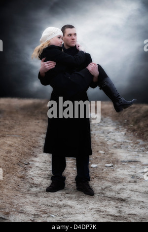 a man carries his girlfriend over a meadow Stock Photo