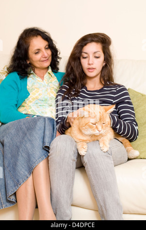 Mother and Teenage Daughter having a Difficult Conversation on the Sofa with the Family Cat Sitting on a Lap Stock Photo