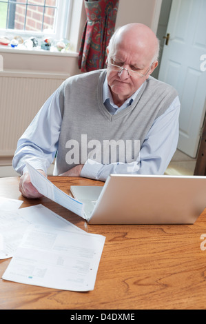 Senior man looking at bills at home with laptop Stock Photo