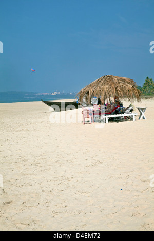 holidaymakers relaxing on secluded tropical beach under shack para glider in distance white sands and ocean Stock Photo
