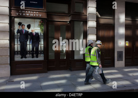 Two manual labourers walk past the Charles Tyrwhitt menswear outfitters at Liverpool Street in the City of London, the capital's heart of its financial district - a good location for suits and businesswear. A pair of Englishmen raise their bowler hats in a gesture from a previous era, when hats said much of your social standing, a summary of your position in the class system. In the 21st century though, the hat is largely an item of clothing to wear only for extreme cold or heat. Stock Photo