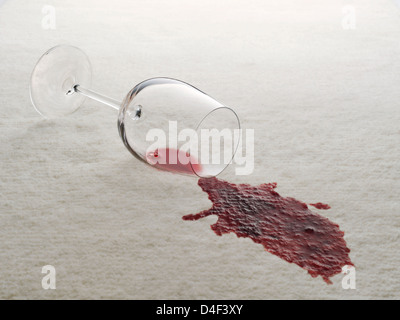 Glass of red wine spilled on white carpet Stock Photo