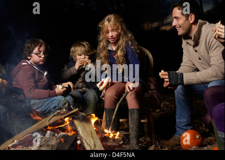 Family eating around campfire at night Stock Photo