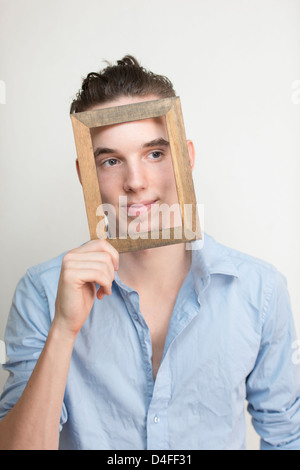 Happy and carefree young adult man posing with wooden frame in front of his face Stock Photo