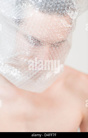 Portrait of anxious young adult male wrapped in transparent plastic. He is looking sad, shy and discontent. Stock Photo