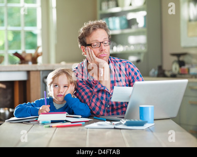Bored father and son working at table Stock Photo