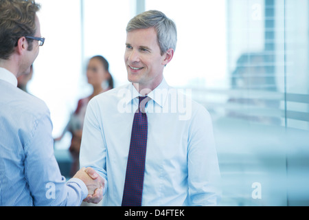 Businessmen shaking hands in office Stock Photo