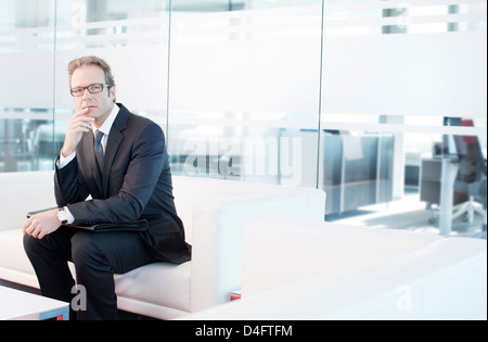 Businessman sitting on sofa in office lobby Stock Photo
