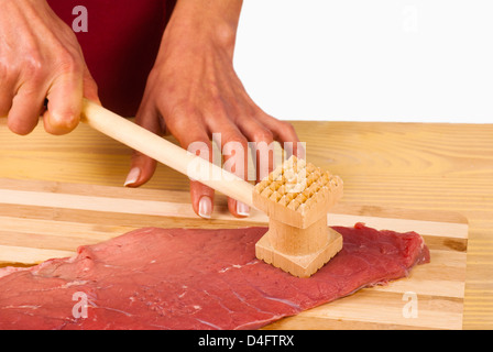 Tenderizing a raw steak with a kitchen hammer Stock Photo