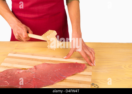 Tenderizing a raw steak with a kitchen hammer Stock Photo