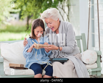Woman giving granddaughter present in porch swing Stock Photo