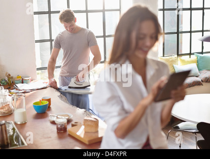 Woman using digital tablet as boyfriend irons in kitchen Stock Photo