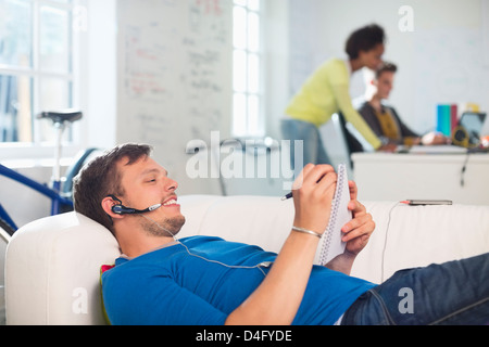 Man in headset taking notes on sofa Stock Photo