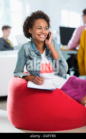 Businesswoman taking notes on phone in bean bag chair Stock Photo