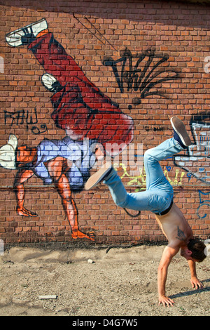 young man doing a hand stand with a grafity break dancer painted on the background Stock Photo
