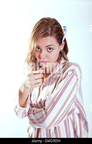 young beautifull woman earging you to brush teeth pointing finger to the camera and with tooth brush behind the ear Stock Photo