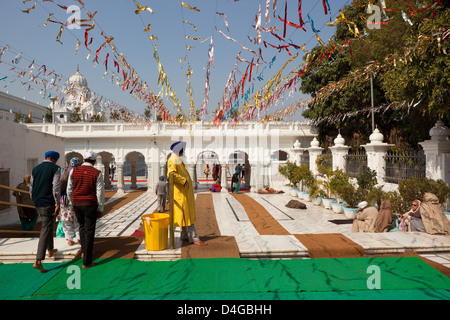 One of the four entrances to the Golden Temple in Amritsar India with people, a temple guard and foil bunting under a blue sky Stock Photo