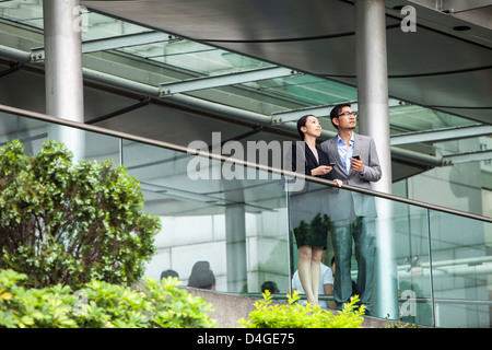 Asian businessman and businesswoman with smart phones, standing on a walkway in Hong Kong. Stock Photo