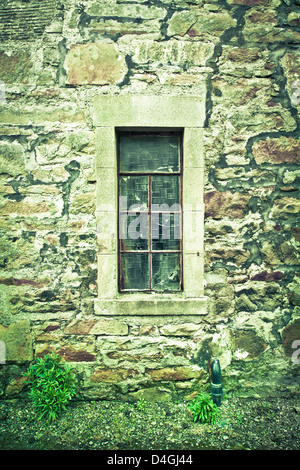 A cracked window in a derelict stone cottage Stock Photo