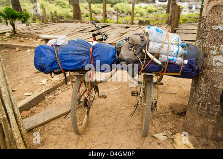 Two dusty, heavily laden touring bikes lean against a tree Stock Photo