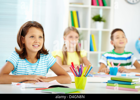 Portrait of lovely girl and her two schoolmates on background looking at something attentively at lesson Stock Photo