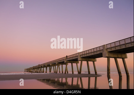 Florida's Jacksonville Beach Pier bathed in the beautiful dusk-colored pastels of the open sky and reflecting water beneath. USA Stock Photo