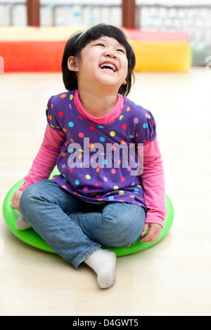 Laughing girl on a big toy dreidel in kindergarten Stock Photo