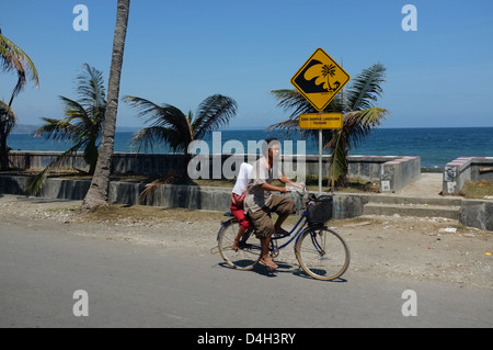 Boy cycling past a tsunami warning sign in Pangandaran, West Java, Indonesia Stock Photo