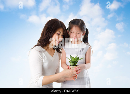 Happy Asian young mother with daughter taking care plant in summer day, blue sky as background. Stock Photo