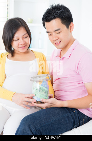 Asian family financial planning concept. Young pregnant couple saving money for future. Living lifestyle at home. Stock Photo