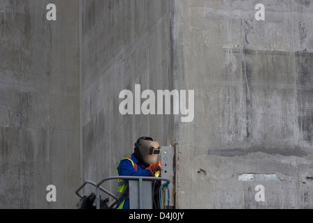 A welder works high up from the ground from the safety of a hydraulic platform on the side of a lift shaft being constructed on a large development project on London Wall in the City of London, the capital's financial district - also known as the Square Mile. With the visor of his helmet lit by the glow from his acetylene torch, the man leans towards the detail of this close-up contact job. Oxy-fuel welding (commonly called oxyacetylene welding, oxy welding, or gas welding in the U.S.) and oxy-fuel cutting are processes that use fuel gases and oxygen to weld and cut metals, respectively. Stock Photo
