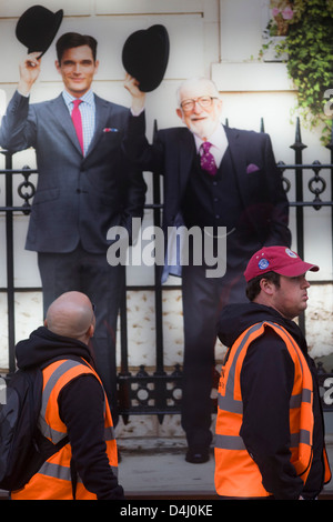 Two manual labourers walk beneath a poster for the Charles Tyrwhitt menswear outfitters at Liverpool Street in the City of London, the capital's heart of its financial district - a good location for suits and businesswear. A pair of Englishmen raise their bowler hats in a gesture from a previous era, a bygone gentlemanly tradition. when hats said much of your social standing, a summary of your position in the class system. In the 21st century though, the hat is largely an item of clothing to wear only for extreme cold or heat. Stock Photo