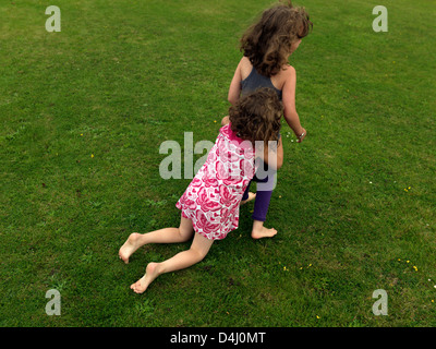 Sisters One Hugging The Others Legs As She Is Trying To Walk In Garden England Stock Photo