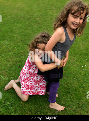 Sisters One Hugging The Others Legs As She Is Trying To Walk In Garden England Stock Photo