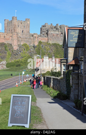 The town centre of Bamburgh, with the castle behind, in Northumberland, northern England, UK Stock Photo