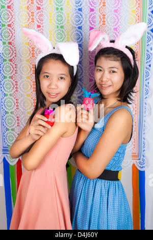 Cute Asian bunny girls hold Easter eggs in front of colorful flower shaped backdrop. Stock Photo