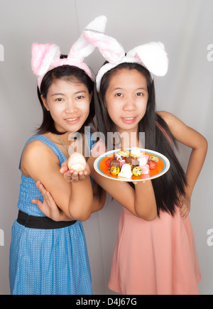 Cute Asian bunny girls hold plate of Easter eggs, chocolate and rock egg. Stock Photo