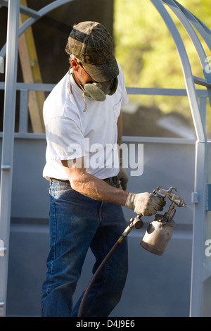 Construction steel worker uses a paint sprayer to apply a primer coat to metalwork. Stock Photo