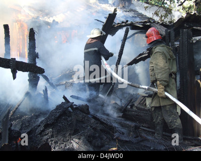 Smoldering remains of a ghetto house with a fireman spraying water firefighters extinguish a fire in an apartment house Stock Photo