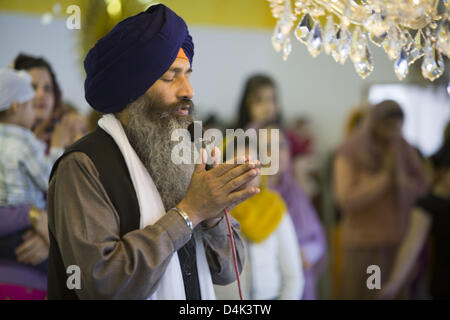 Sikh priest Garanthi Jarnail Singh prays with eyes closed and holding a microphone in front of the Granth, the sacred scripture of Sikhism, in Munich, Germany, 22 March 2009. Turban, beard and bracelet are the visible signs of being a Sikh, taking off shoes in the temple and abdication of indulgence food are established rules of the Sikh. Sikhism denies the worshipping of gods resp Stock Photo